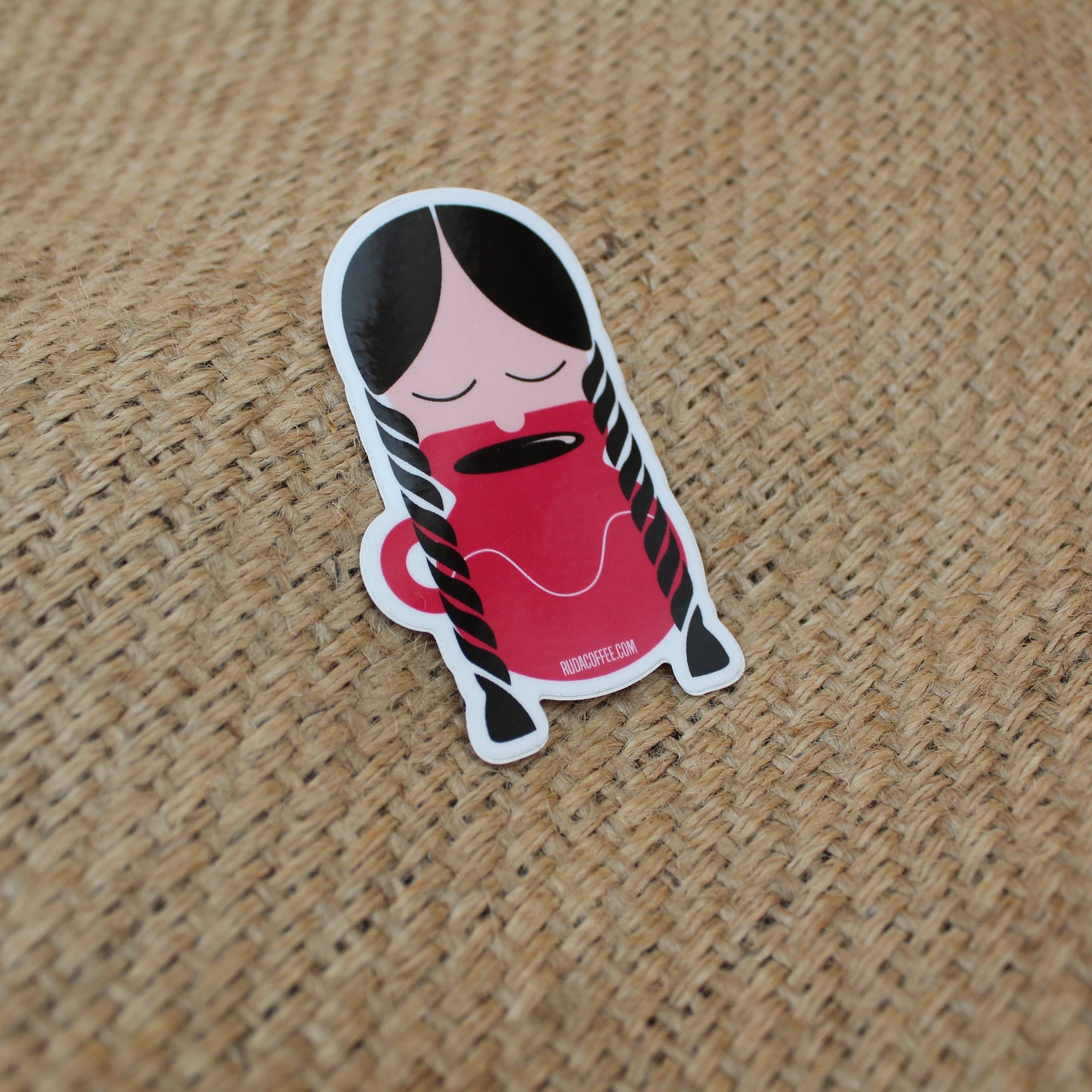 Sticker of a cartoon character holding a red cup on a textured brown surface